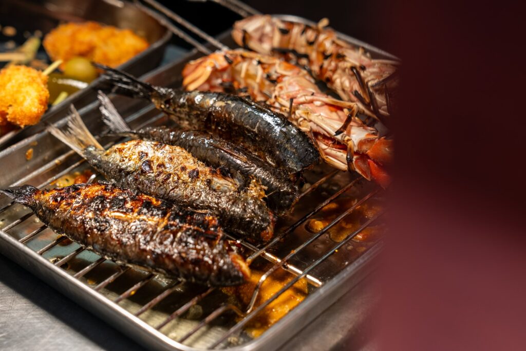 Whole grilled fish and langoustines cooking on a grill.