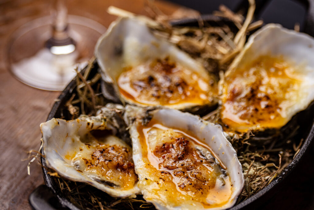 Four grilled oysters in their shells with a golden butter sauce