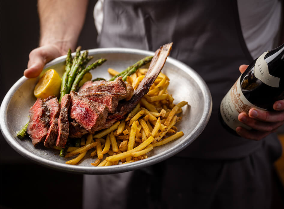 A steak and chips dish with a bottle of wine