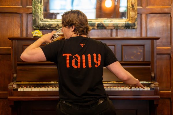 Tallyman team member playing the piano while drinking a pint of beer
