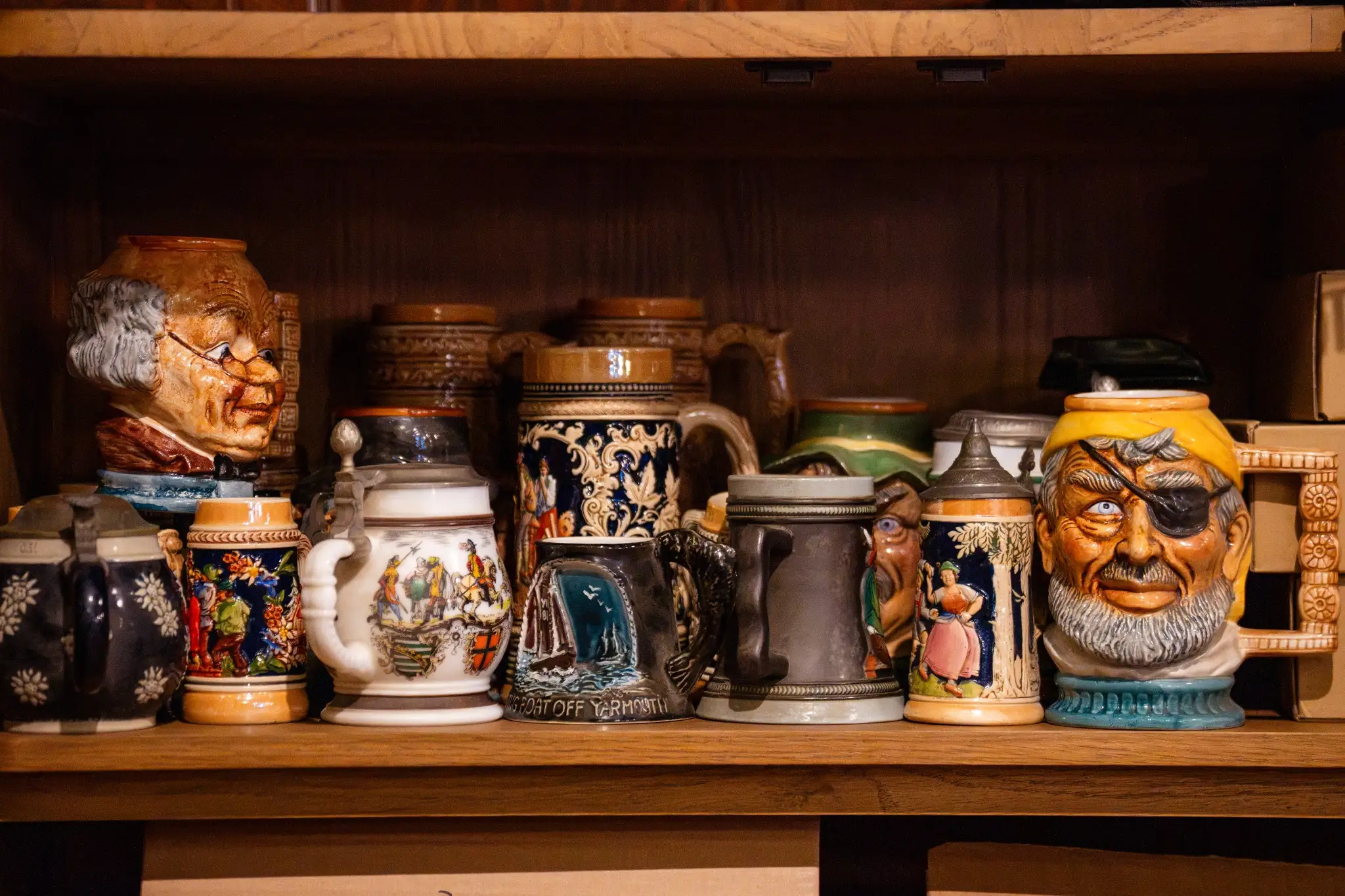 Collection of decorative ceramic beer steins displayed on a wooden shelf.