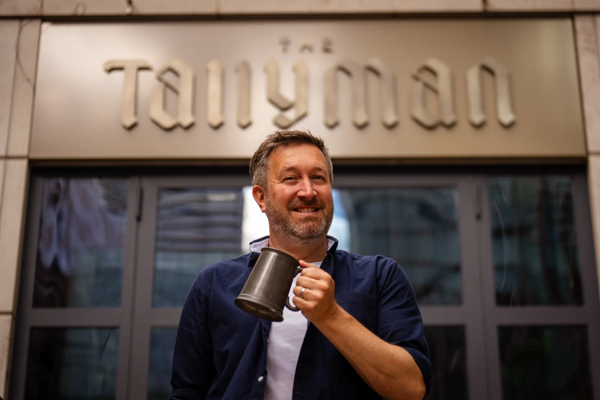 Man holding a metal tankard outside The Tallyman.