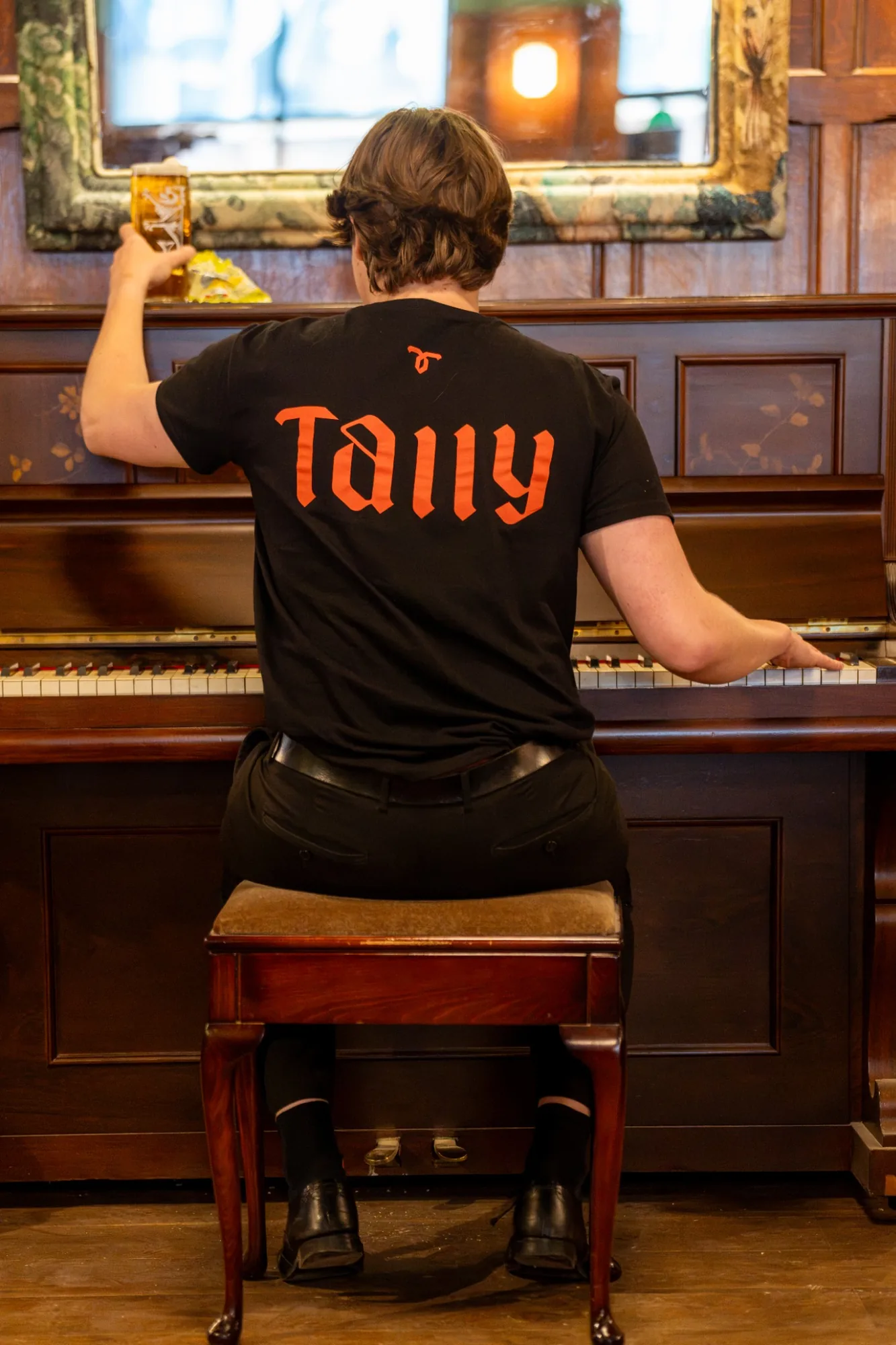 Tallyman team member playing the piano while holding a pint of beer