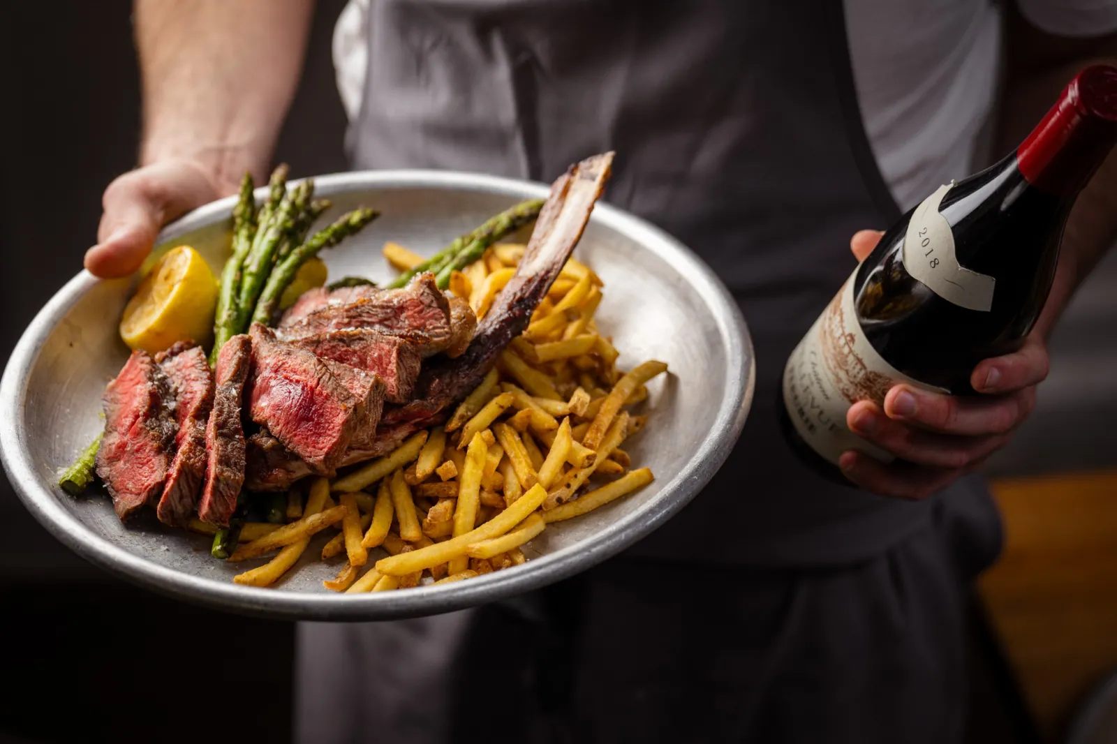 Sliced steak with fries, asparagus and lemon being served with a bottle of red wine at The Tallyman