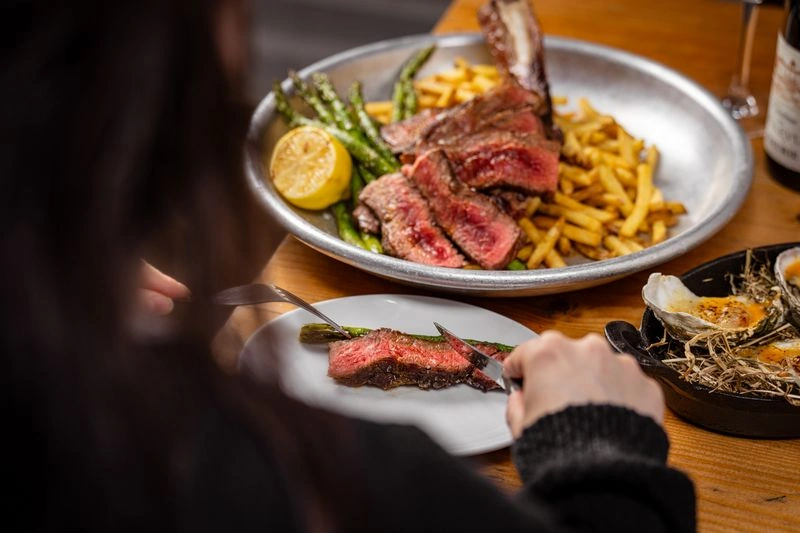Guest eating sliced steak with fries, asparagus and oysters at The Tallyman.